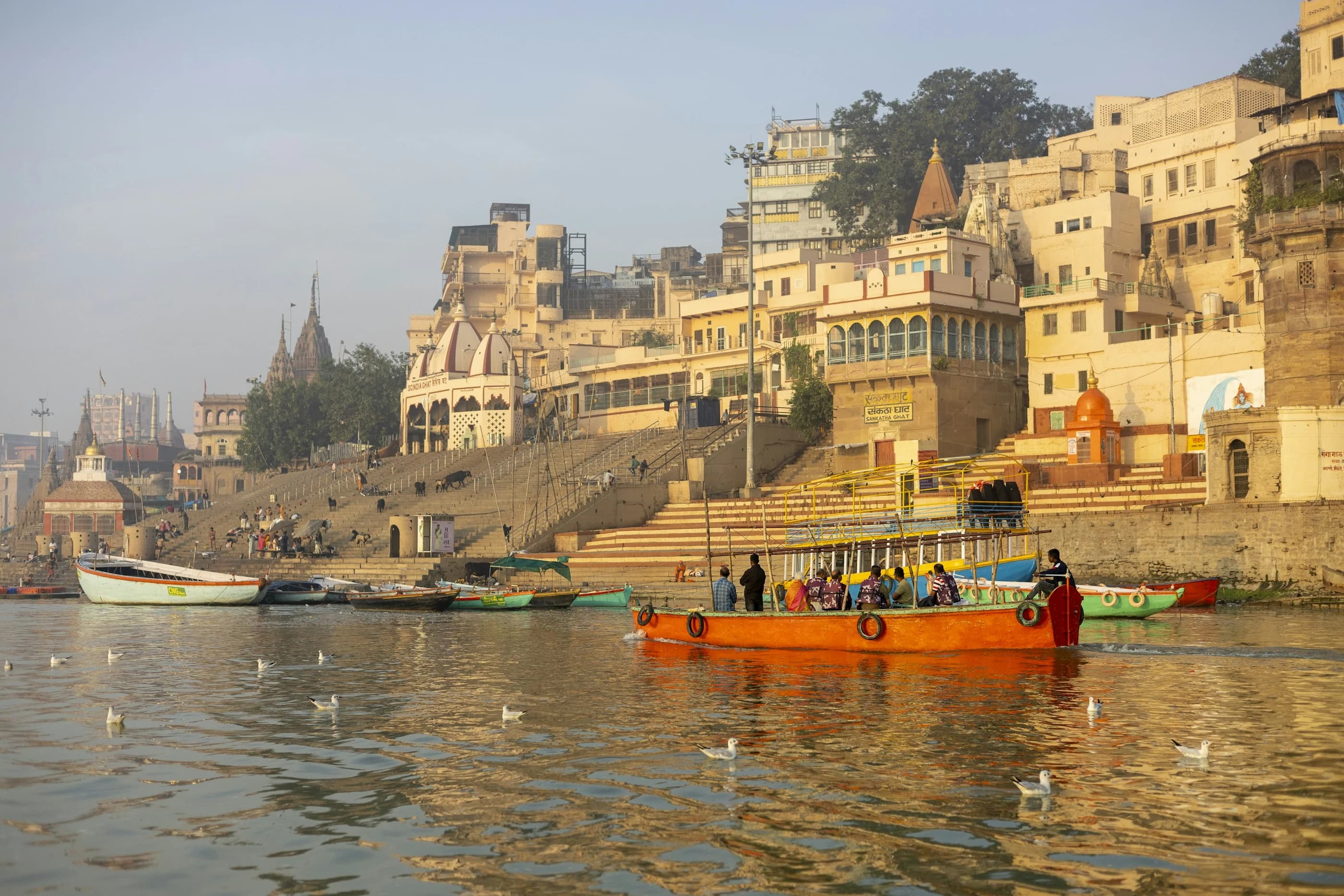 Boats on the Ganga beside the sunlit ghats and buildings of Varanasi